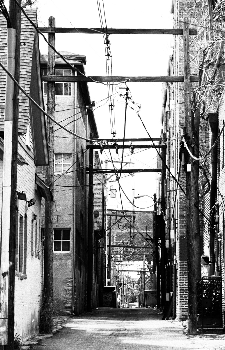 Black and white photograph of an alley strung with power lines, titled The Alley of Decision.