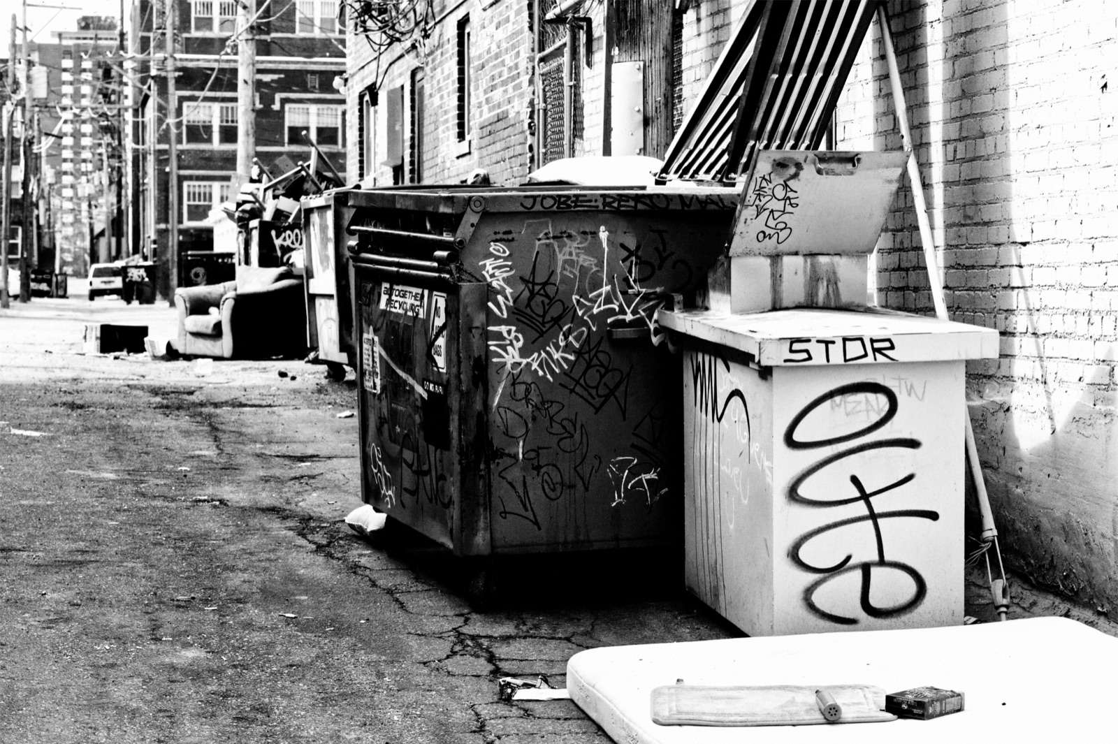 Black and white photograph of a graffiti-covered dumpster in an alley, titled Discarded Memories.